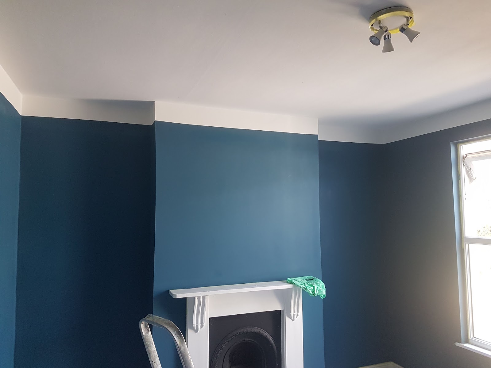 A living room painted in deep teal with a crisp white ceiling and fireplace